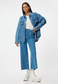 Camisa de denim azul oversized con bolsillos frontales, combinada con pantalones de denim azul de talle alto acampanados y botas de plataforma blancas chunky.