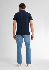 Navyblauwe polo met korte mouwen, met een kraag, gecombineerd met lichtblauwe jeans en witte sneakers. Glad materiaal, casual pasvorm.