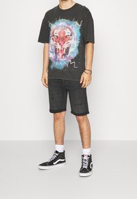La camiseta gráfica negra presenta un diseño colorido de tigre, combinada con pantalones cortos de mezclilla negra desgastados y zapatillas altas negras.