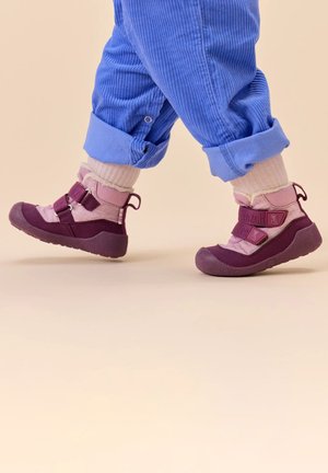 Purple and pink hiking boots with Velcro straps and textured soles, paired with light blue corduroy pants and white socks.