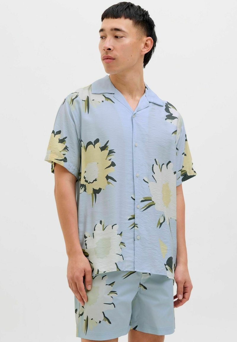 Kortærmet skjorte med knapper i lyseblå med store blomster mønstre i creme og grøn. Sæt sammen med matchende lyseblå shorts.