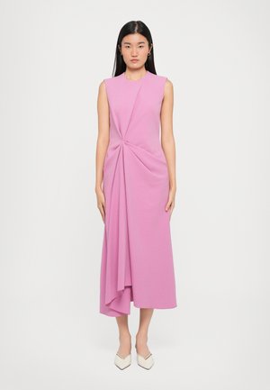 Pink sleeveless dress with a twisted design at the waist, a flowy silhouette, and a below-the-knee length. Worn with white pointed-toe shoes.