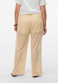 Beige spissebukser med vide ben, med sirkulære utskjæringsmønstre og en teksturert finish. Elastisk midje.