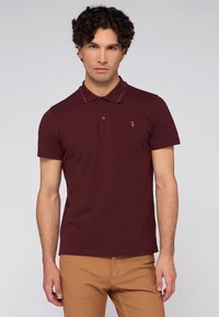Bordová polo košile s dvoupolohovým knoflíkem, oranžovým lemem límce a malým logem na levé hrudi. Měkký bavlněný materiál, krátké rukávy.