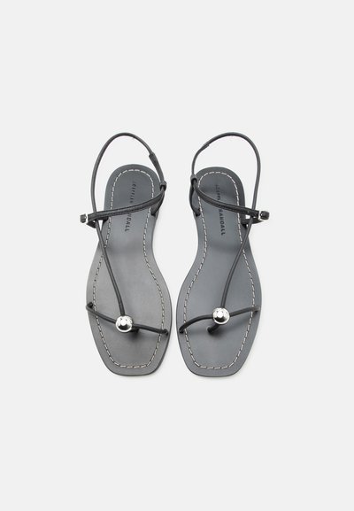 Μαύρα επίπεδα σανδάλια με λεπτές λουρίδες, ασημένια λεπτομέρεια με χάντρες στο δάχτυλο, αγκράφα στον αστράγαλο και λευκή ραφή στις άκρες της σόλας.