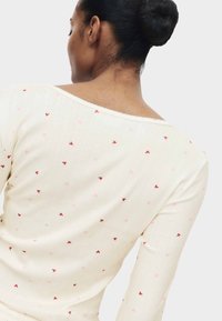 Krämfärgad stickad topp med vid halsringning, med ett texturerat mönster och utspridda små rosa och röda hjärtmönster.