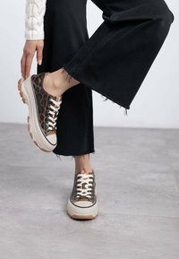 Zapatillas de lona con estampado de leopardo, suela de goma beige y cordones blancos. Combinadas con jeans negros acampanados con dobladillo deshilachado.