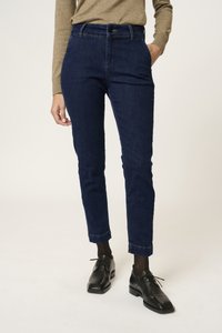 Sötétkék farmernadrág slim fit szabásban, magas derekú, két elülső zsebbel és felhajtott szárakkal, fekete fűzős cipővel párosítva.