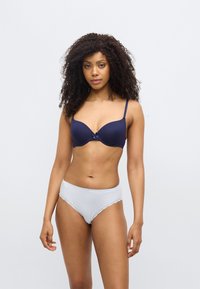 Σκούρο μπλε σουτιέν με απαλή ύφανση, ενίσχυση και κεντρικό φιόγκο· συνοδευόμενο από ανοιχτό γκρι εσώρουχα με δαντέλα και μικρό φιόγκο.