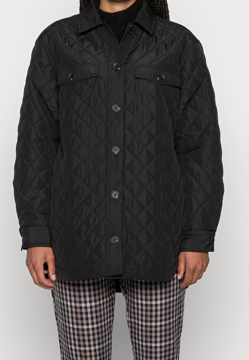 Black quilted jacket with snap buttons, two chest pockets, and a collar. Worn over checkered pants with a contrasting pattern.
