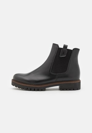Black leather ankle boot with elastic side panels, textured fabric, a loop at the heel, and a rugged traction sole.