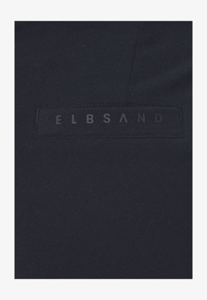 Dunkelblauer Stoff mit einem aufgenähten rechteckigen Patch, der den Schriftzug "ELBSAND" in subtil erhabenen Buchstaben zeigt.
