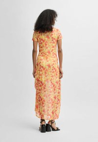 Yellow and orange floral maxi dress with short sleeves, sheer fabric, and a relaxed fit, paired with black strappy heels.