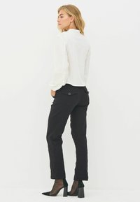 Hvid bluse med ribbet tekstur på ærmerne, parret med sorte tætsiddende bukser. Sorte stiletto hæle fuldender outfittet og fremhæver en slank silhuet.