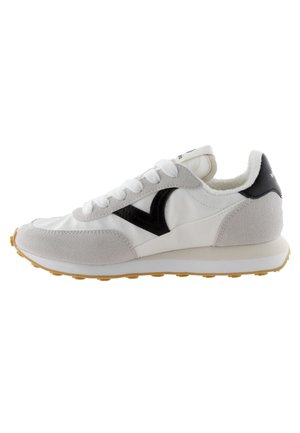 Zapatilla blanca con acentos de ante gris, logo negro y lengua texturizada. Presenta una suela de goma voluminosa con un patrón amarillo. Diseño clásico con cordones.