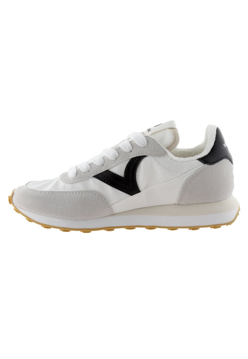 Zapatilla blanca con acentos de ante gris, logo negro y lengua texturizada. Presenta una suela de goma voluminosa con un patrón amarillo. Diseño clásico con cordones.