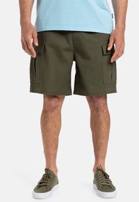 Olivengrøn cargo-shorts med sidelommer, lavet af bomuldsstof og med lige snit; parret med grå sneakers og en lyseblå t-shirt.