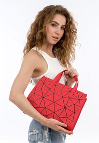 Borsa a spalla geometrica rossa con un motivo triangolare e linee nere. Realizzata in materiale sintetico, presenta manici superiori doppi ed è di forma rettangolare.