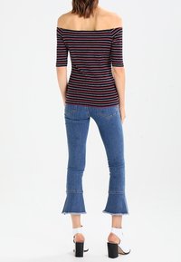 Top de rayas azul marino y rojo, sin hombros y de manga corta, combinado con jeans acampanados de color azul claro y sandalias de tacón cubano blanco.