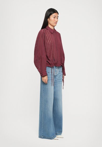 Burgundy striped blouse with a collar and drawstring hem, paired with wide-leg light blue jeans. Smooth texture and relaxed fit.