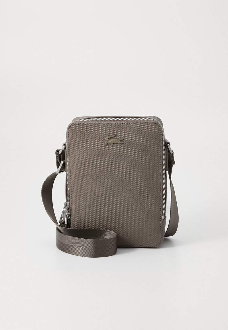 Tekstūrēta pelēka sintētiska crossbody soma ar taisnstūrveida formu, ar rāvējslēdzēja aizdari, regulējamu siksnu un iegriezta logotipa detalizāciju.