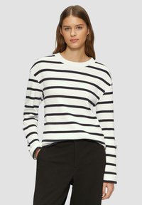 Maglione bianco con strisce orizzontali nere, texture a coste, scollatura rotonda e maniche lunghe, abbinato a pantaloni neri.