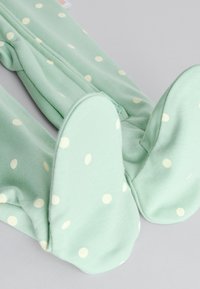 Menta zöld baba body fehér pöttyökkel, lábakkal és elöl végig cipzárral, szürke háttéren.