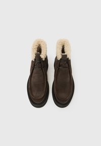 Braune Wildleder-Stiefeletten mit weichem, cremefarbenem Kunstpelzbesatz, schwarzen Schnürsenkeln und einer strukturierten Sohle für besseren Halt.