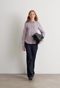 La modella indossa una camicia a righe con colletto, abbinata a jeans svasati blu scuro. Tiene in mano una borsa a tracolla in pelle nera.