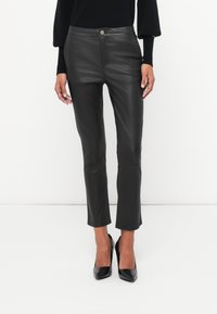 Čierne, syntetické kožené nohavice slim fit s vysokým pásom, minimalistickými prednými detailmi a skráteným lemom, doplnené čiernymi vysokými podpätkami.