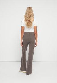 Pantalons évasés marron en tissu doux avec une texture côtelée, dotés d'une taille élastique et d'un léger stretch pour le confort.
