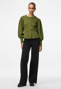 Zielony żeński kardigan w prążki z bufiastymi rękawami, z metalowymi guzikami z przodu, w zestawieniu z czarnymi spodniami typu wide-leg i czarnymi butami.