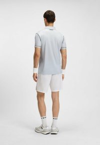 Polo shirt grigio chiaro con colletto strutturato, dettagli in bianco e nero, abbinato a pantaloni corti bianchi. Il modello indossa scarpe sportive grigie e calzini.