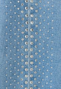 Tissu en denim bleu avec une couture verticale décorée de petits et grands clous ronds argentés disposés en motifs symétriques.
