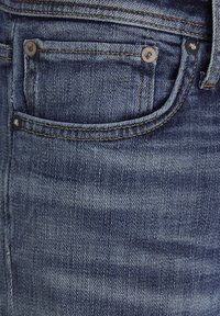 Tessuto in denim blu scuro con finitura testurizzata, dotato di cuciture gialle, una piccola tasca anteriore e due rivetti metallici.