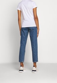Camiseta blanca de algodón con mangas remangadas, combinada con jeans de mezclilla azules. Las zapatillas presentan un diseño en beige con acentos en azul marino. Líneas limpias y ajuste casual.