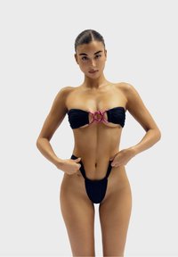 Zwarte bikini set met een bandeau top met een roze accent en ingewikkelde details. Dunne bandjes en een ontwerp met minimale bedekking voor de onderkant.
