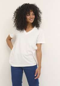 T-shirt bianco a scollatura a V realizzato in tessuto morbido, con maniche corte e vestibilità rilassata. Abbinato a jeans in denim blu.