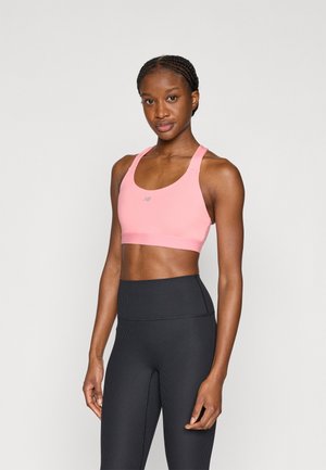 Rózsaszín sportmelltartó lekerekített nyakkivágással és széles pántokkal, fekete, bordázott, magas derekú leggingsszel párosítva. Mindkettő testhezálló szabású.