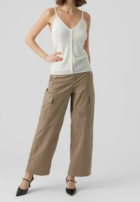 Top in cotone bianco a costine con dettaglio a bottoni abbinato a pantaloni cargo beige larghi con tasche laterali, indossato con décolleté nere a punta.