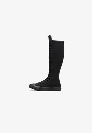 Mustavad kõrged kanvassaapad, millel on ümar nina, tõmblukk ja esikinnitus. Omab tekstuurset pinda ja kummist tallat.