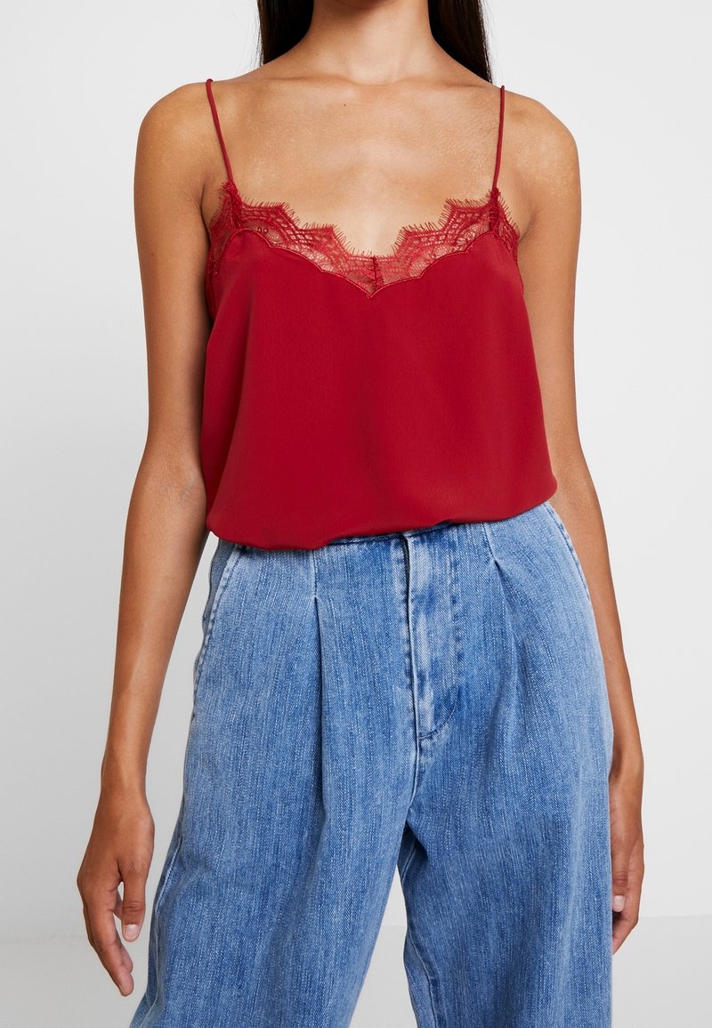 Camisola di seta rossa con scollo in pizzo, dotata di spalline regolabili, abbinata a pantaloni in denim a vita alta di colore azzurro chiaro.