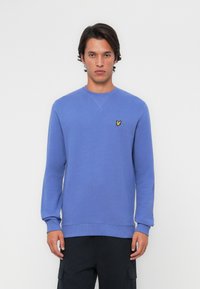 Lyseblå crewneck sweatshirt laget av mykt stoff, med en liten gul sommerfugl-logo på brystet og ribbestrikkede mansjetter og hem.