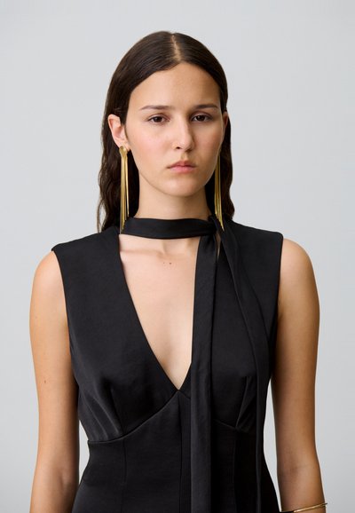 Vestido negro sin mangas con un escote en V profundo y un detalle de bufanda atada en el cuello. Textura suave, silueta ajustada y sin patrones visibles.