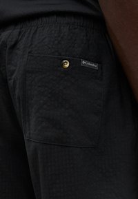 Pantalon noir texturé avec taille élastique et poche arrière boutonnée ornée d'une étiquette de la marque Columbia.