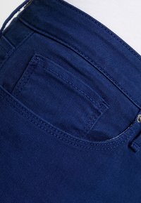 Tejido de mezclilla azul marino, con un bolsillo trasero con costuras detalladas. Acabado limpio, cinturilla estándar y textura sutil visible.