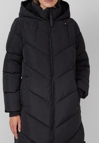 Zwarte pufferjas met een chevronpatroon, capuchon met nepbontvoering, ritssluiting aan de voorkant en elastische manchetten voor extra warmte.