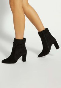 Black suede ankle boots with a slouchy cuff, pointed toe, and block heel. Features a zip closure on the side for easy wear.