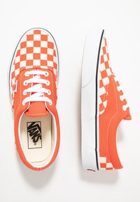 Vans ternede sneakers med en orange kanvas-overdel og et hvidt ternet mønster, hvide snørebånd og en hvid gummisål.