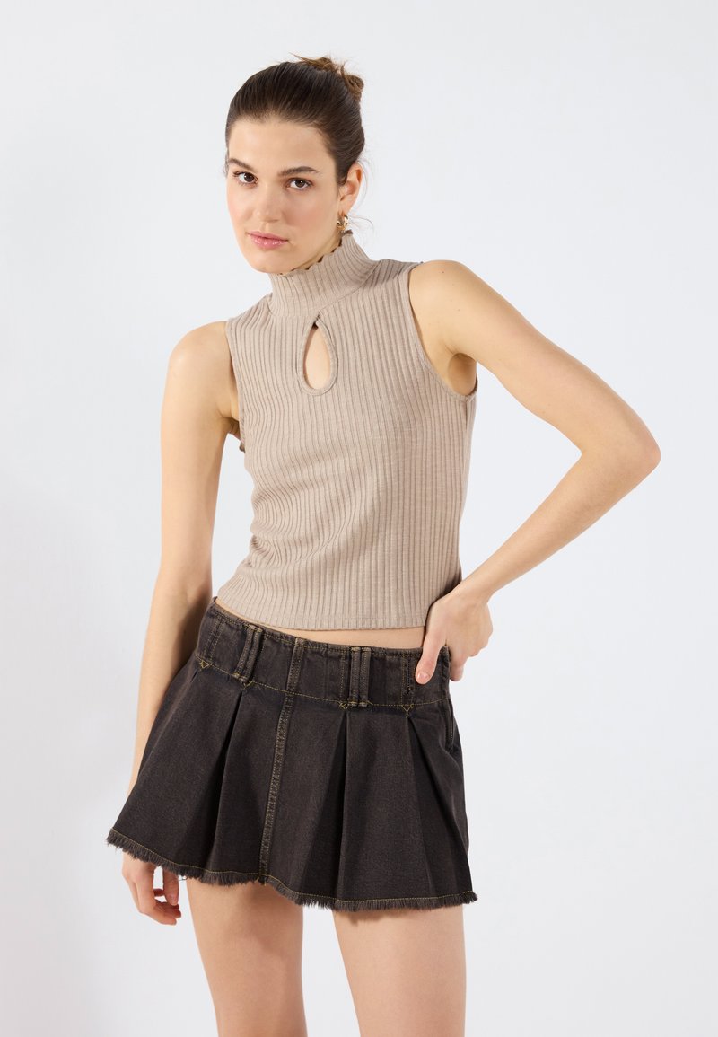 Beige ribbad ärmlös topp med nyckelhål, tillsammans med en svart denimminikjol med veck och fransad fåll.